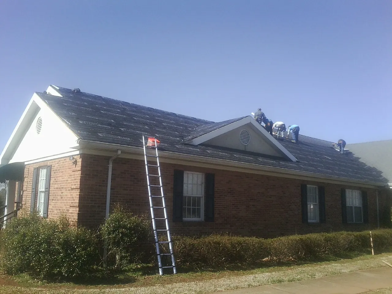 Crew tearing shingles off a brick ranch roof with a ladder set — Emergency Roof Repair work by our crew in Centerbrook