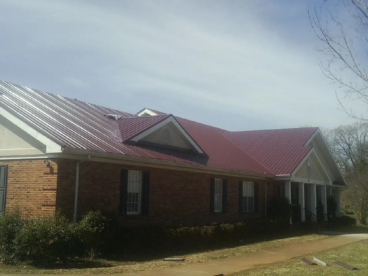 Red metal roof with gabled entries on a long brick building, from a Hail Damage Roof Repair job in Centerbrook