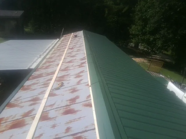 Old rusted panels beside newly installed green metal roofing — Wind Damage Roof Repair by Roofing Brothers in Centerbrook