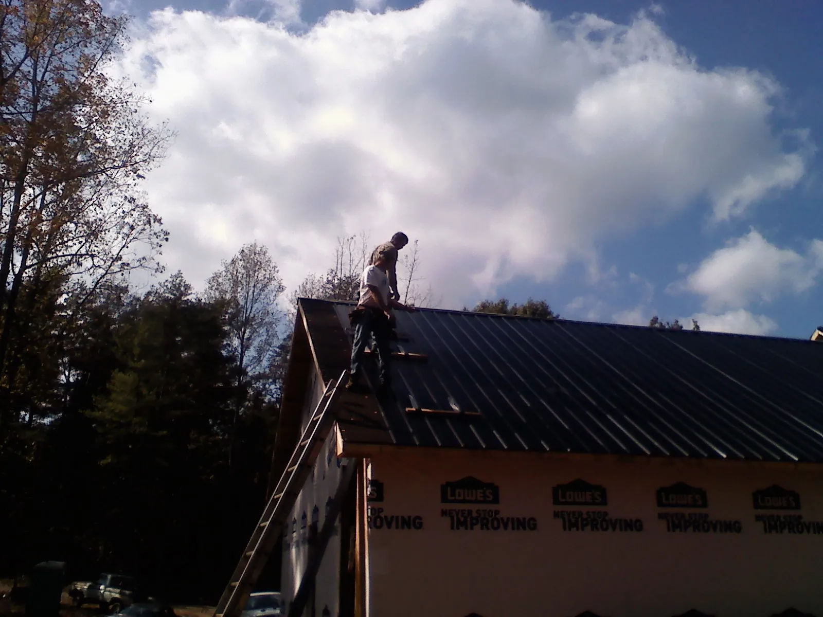 Roofer fastening dark metal panels high against a cloudy sky, from a Roof Inspection job in Centerbrook