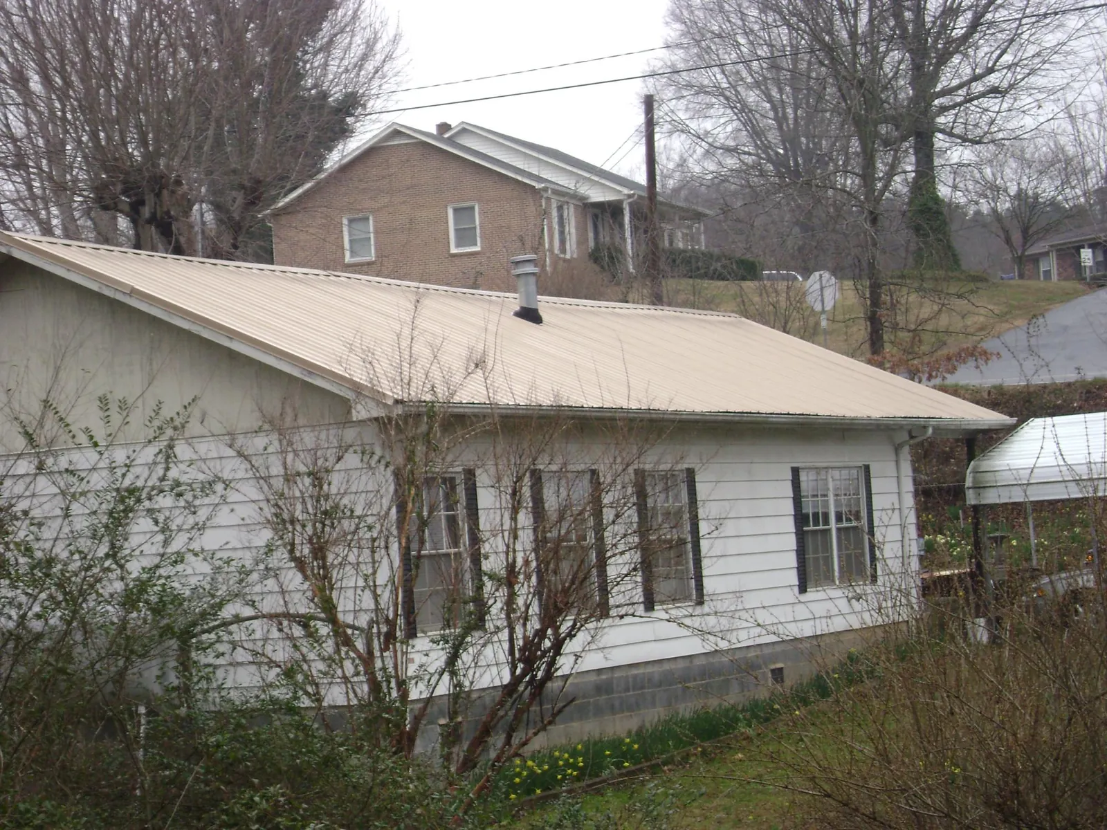 Tan metal roof on a white sided house set into a hillside — Commercial Roofing by Roofing Brothers in Centerbrook